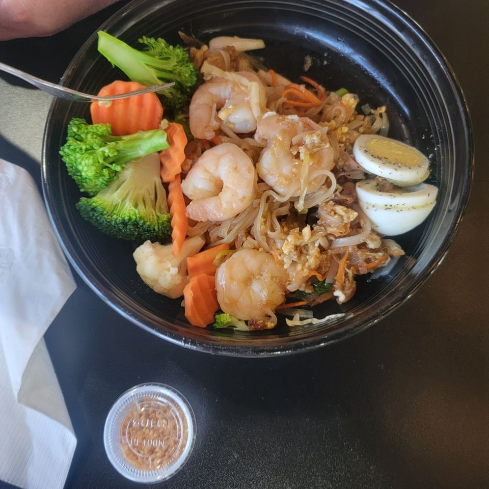 Rice & Bites shrimp pad thai with broccoli, carrots, and hard-boiled eggs in a black bowl.