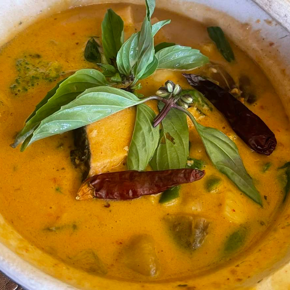 Close-up of Rice & Bites' yellow curry with basil leaves, dried chilies, and vegetables.