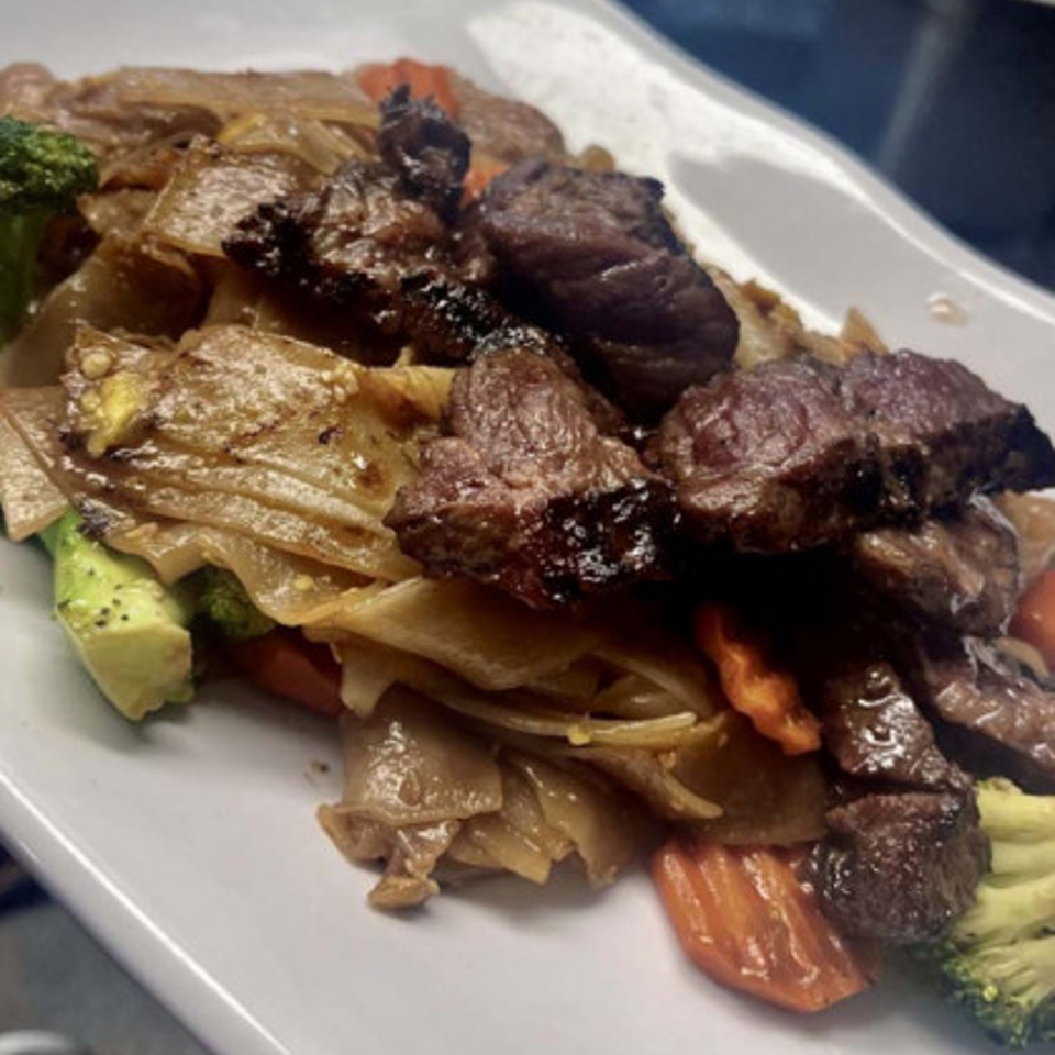 Rice & Bites' beef and noodle dish with broccoli, carrots, and avocado on a white plate.