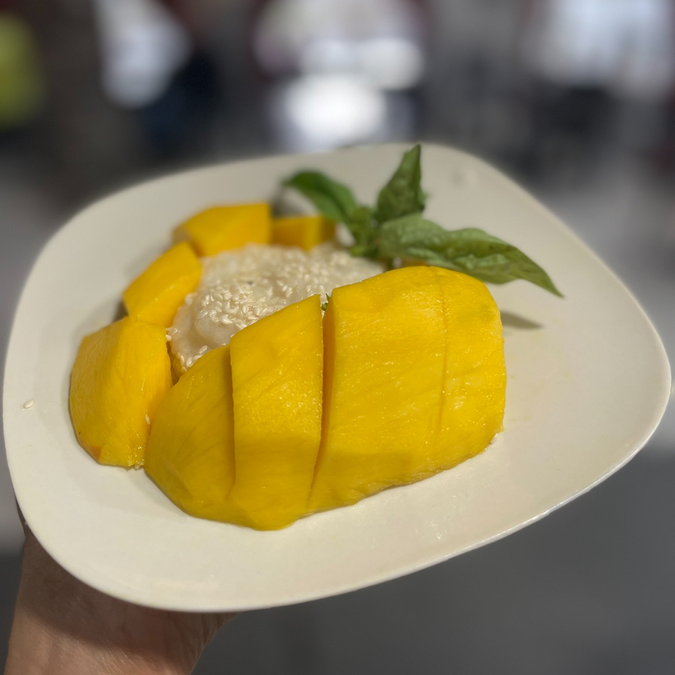 Mango sticky rice dessert with sesame seeds and a mint garnish on a white plate.