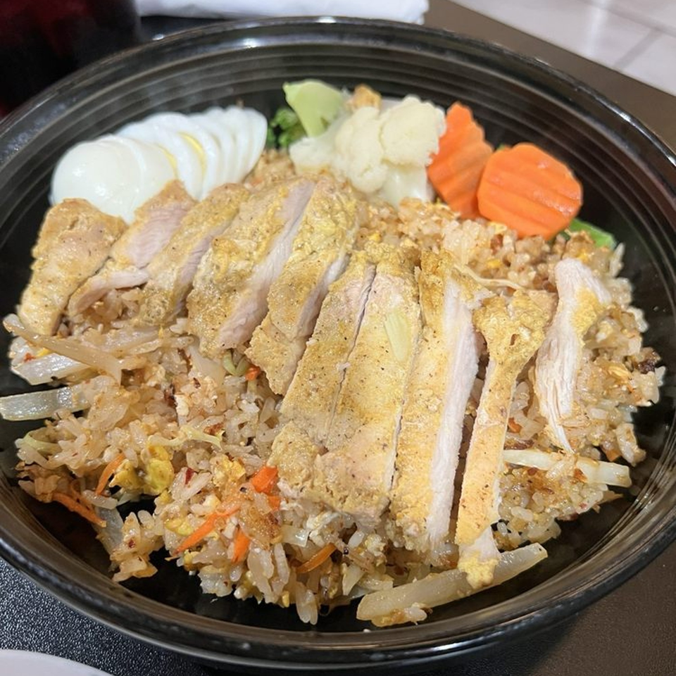 Chicken fried rice with sliced chicken breast, boiled egg, carrots, and pickled vegetables in a black bowl.